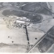 Aerial view from position above Huntington Drive near Holly Avenue intersection looking north over Santa Anita Park.  Colorado Place and Huntington Drive are seen coming together at right side of photo.  Note how small the deodar (?) trees planted along Huntington Drive and Colorado Place are.  Row of trees seen in center of photo were apparently left from Ranch days and were later removed.